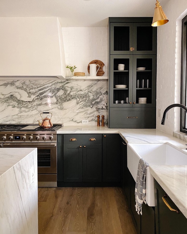 Kitchen with green cabinets, plaster stove vent and floating shelves.