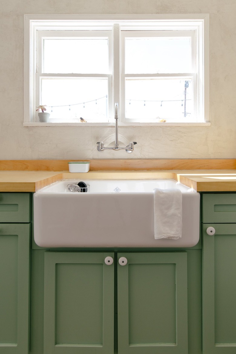 a kitchen includes a deep porcelain sink, green wooden cabinets, and a butcher-block counter