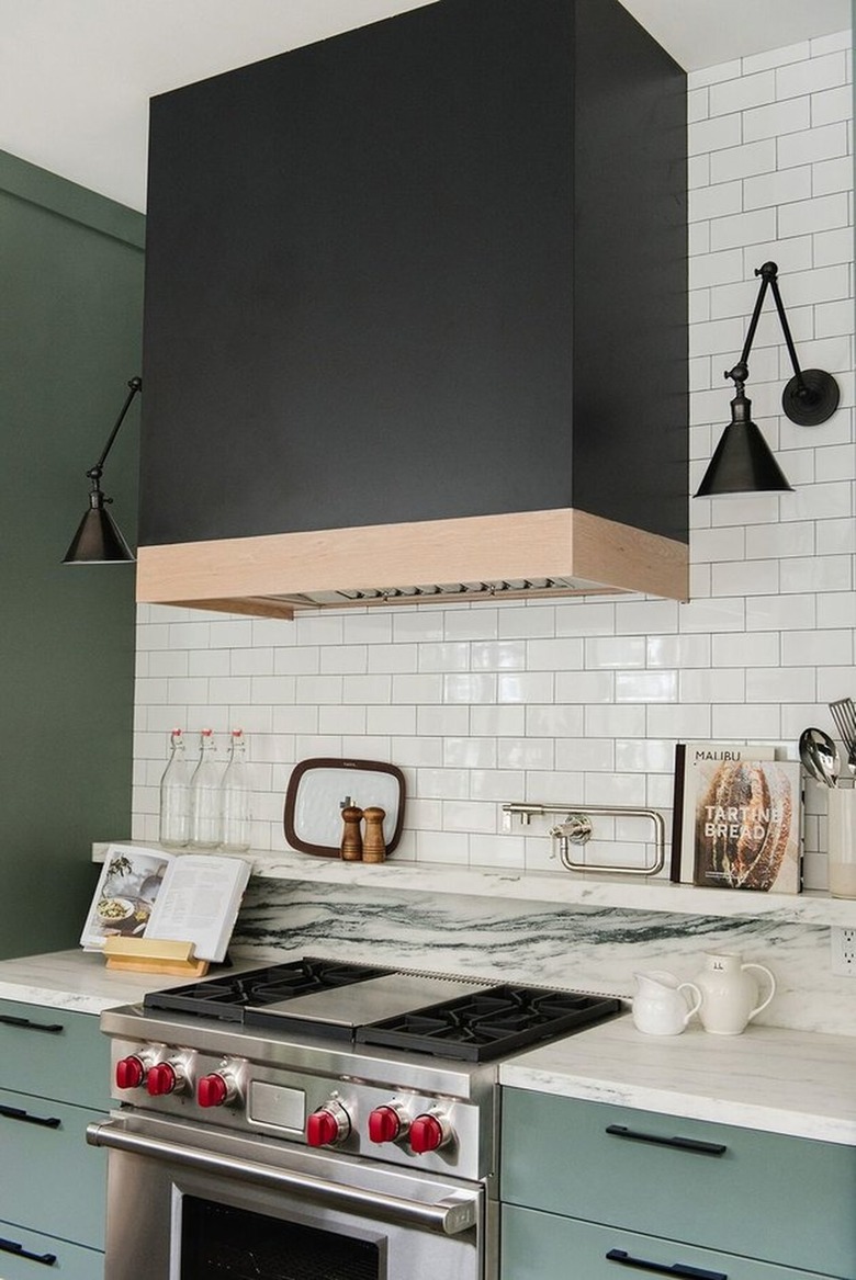 Kitchen with custom black range hood, stainless range, green cabinets.