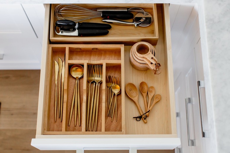 An open cutlery drawer with a wooden organizer, cold cutlery, and various other utensils.