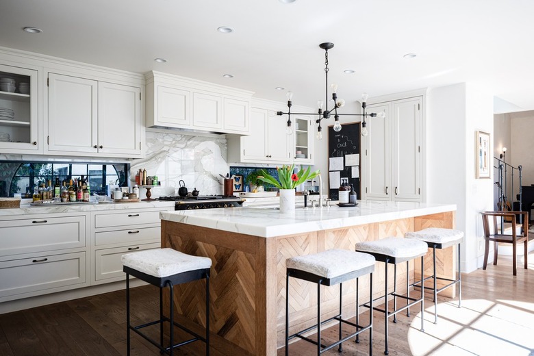 A kitchen with white cabinets, contemporary light fixture and wood kitchen island