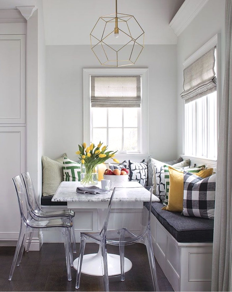 Kitchen nook idea with three clear acrylic chairs at a marble table in a breakfast nook in a white kitchen