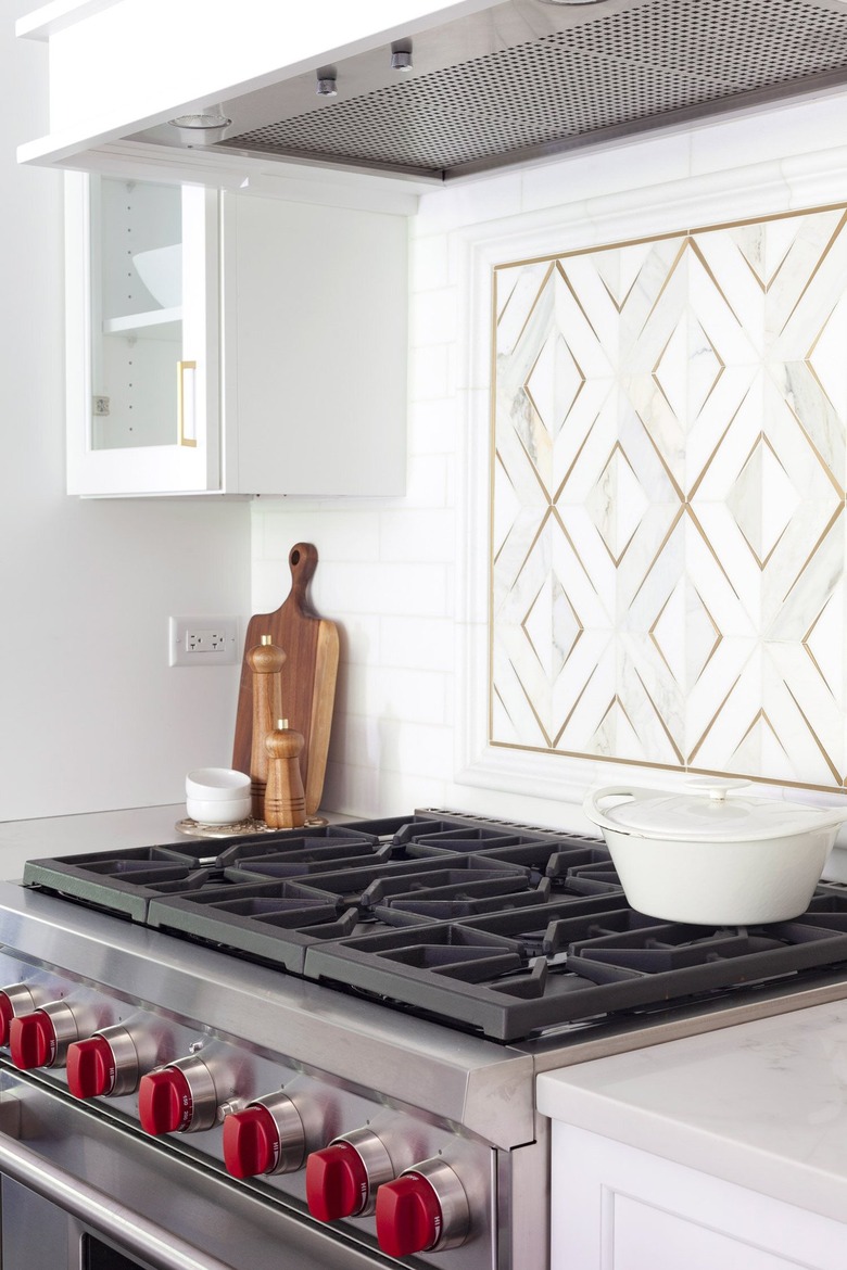 brass and marble backsplash behind stovetop in white kitchen