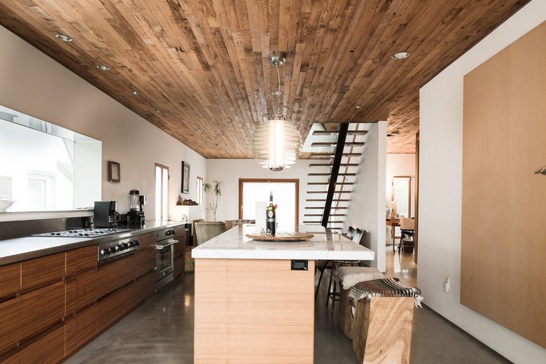 Kitchen with wood cabinets, and a light wood kitchen island. A beehive pendant light hangs from a wood ceiling.