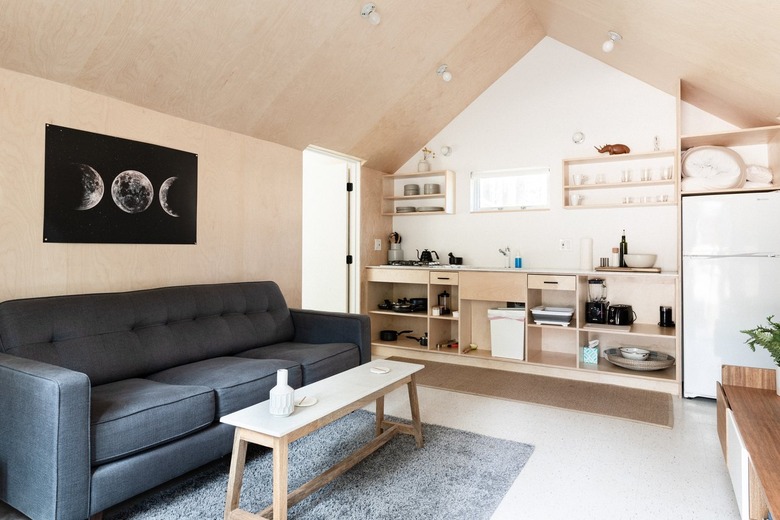 A minimalist living room with wood walls and cabinets with a gray sofa