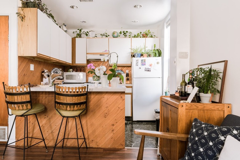 Jungalow kitchen with houseplants, wood-white door cabinets, and a kitchen island with bar stools.