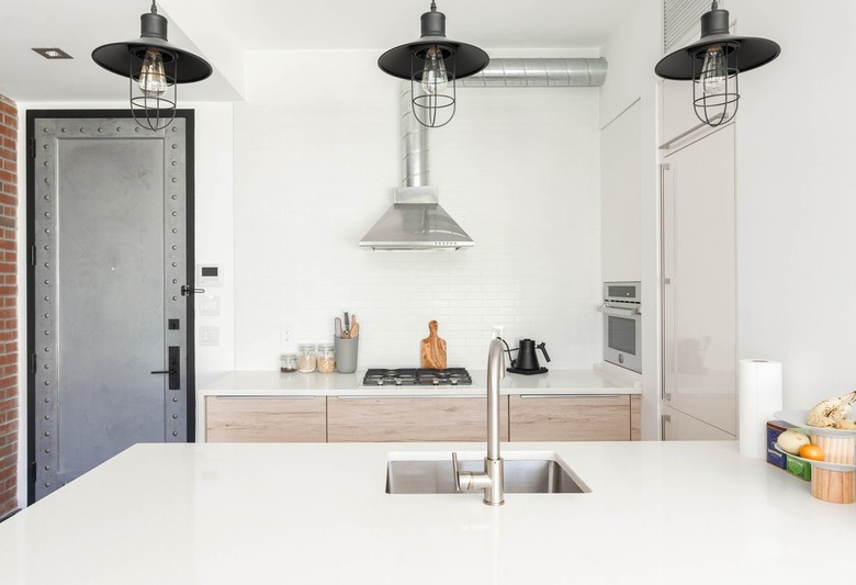 White contemporary kitchen with white countertops, wood cabinets, black stove burners, and silver sink and faucet with black hanging lights