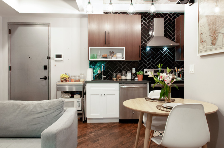 small kitchen with dark chevron tile backsplash, dark wood cabinets, stove and vented range hood