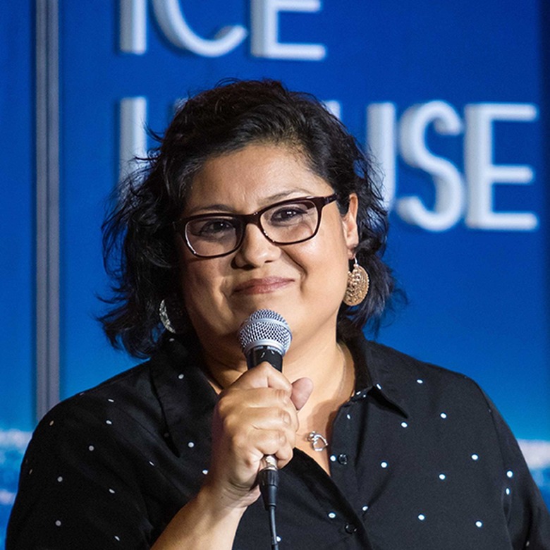 person with glasses holding a microphone, with a blue background with white text