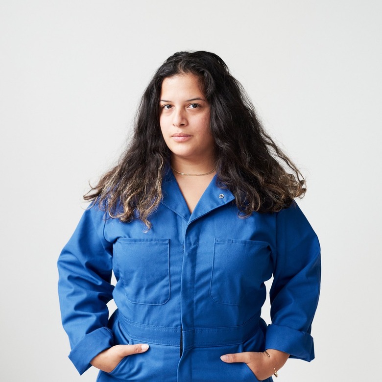 A person with wavy brown hair, wearing a royal blue jumpsuit.