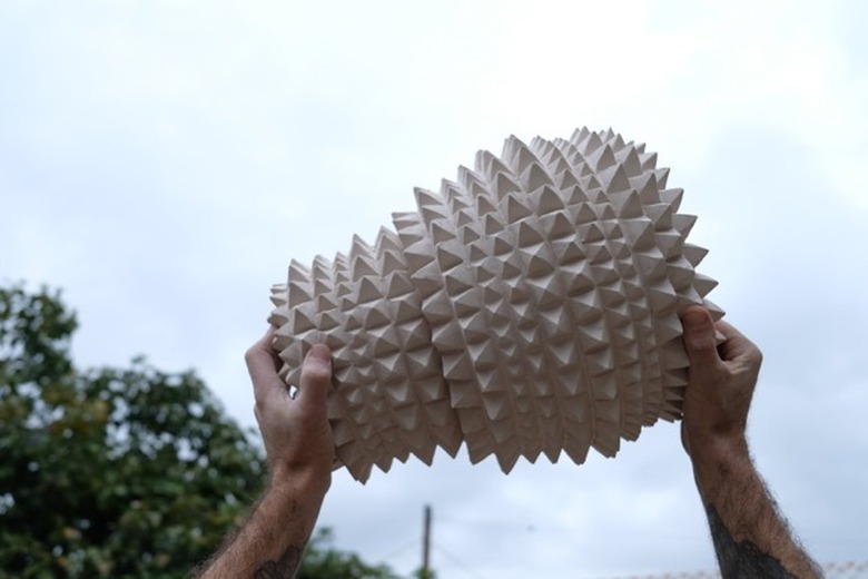 two hands holding up a ceramic piece with the sky and a tree in the background