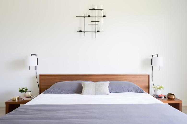 modern bedroom with wall sconces on either side of wood headboard