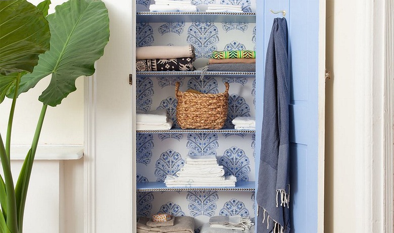 linen closet organization with wallpaper on back wall and painted door