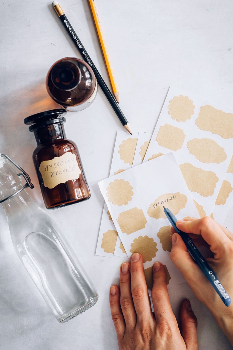 Hand painting gold sticker label sheets for cleaning bottles next to pencils