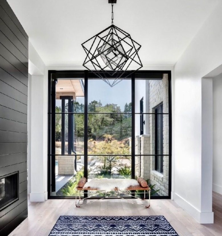 Minimalist living room with geometric chandelier, rug, bench, fire place, large window.