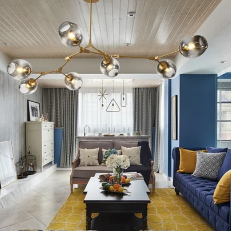 Living room with linear chandelier, blue couch, yellow rug.