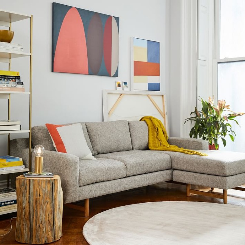 living room rug idea with a round light gray rug in front of a tan sectional, with abstract art behind it on the wall