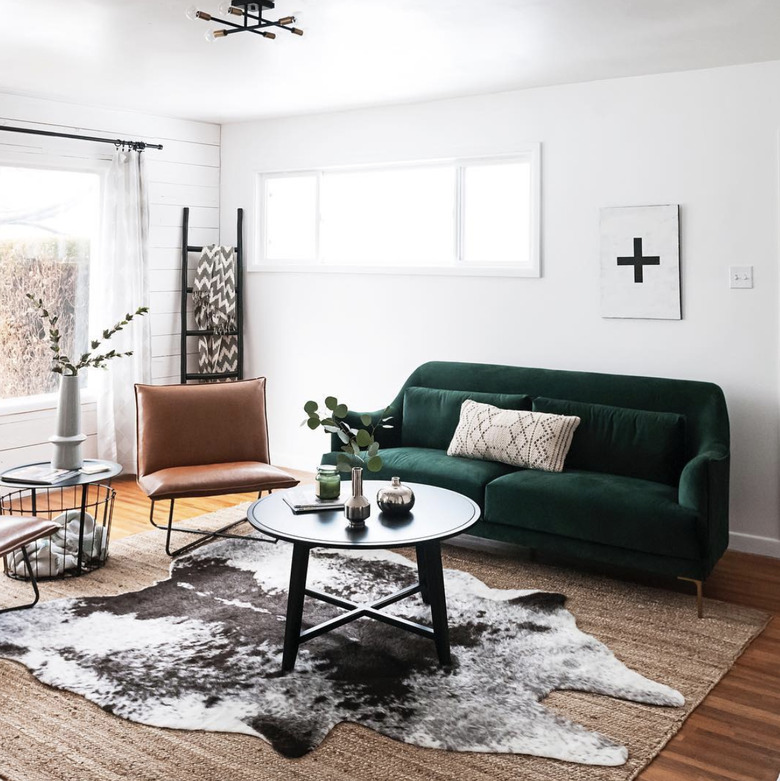 living room rug idea with a green couch in a living room with a small round coffee table, and a brown and white cowhide rug layered over a jute rug