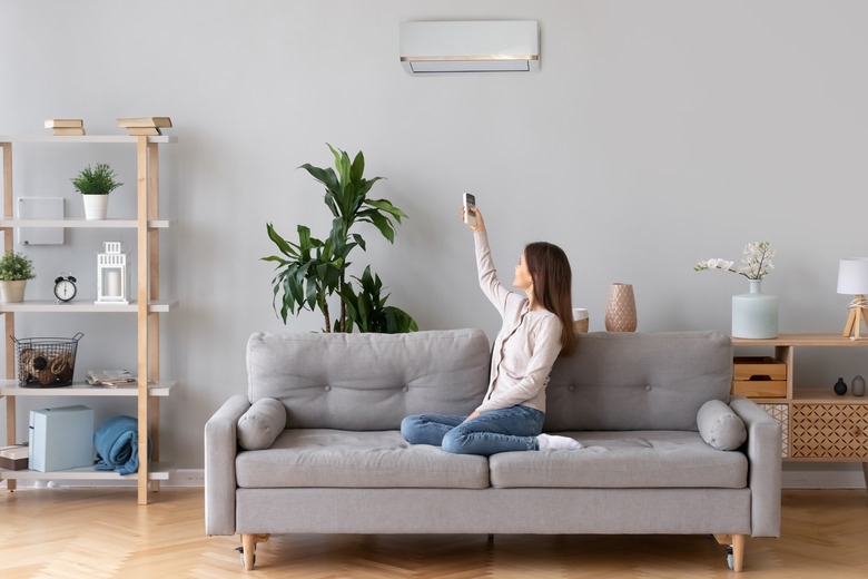 Young woman switching on air conditioner sitting on couch