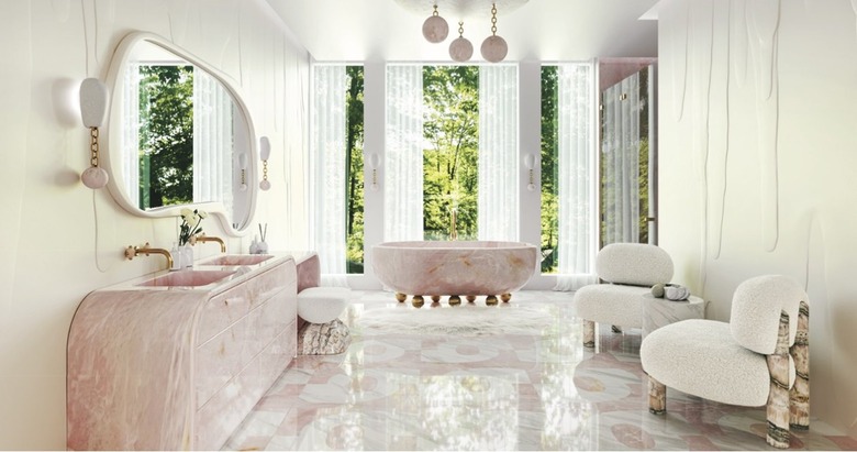 A pink freestanding marble tub with brass orb legs surrounded by a marble bathroom.