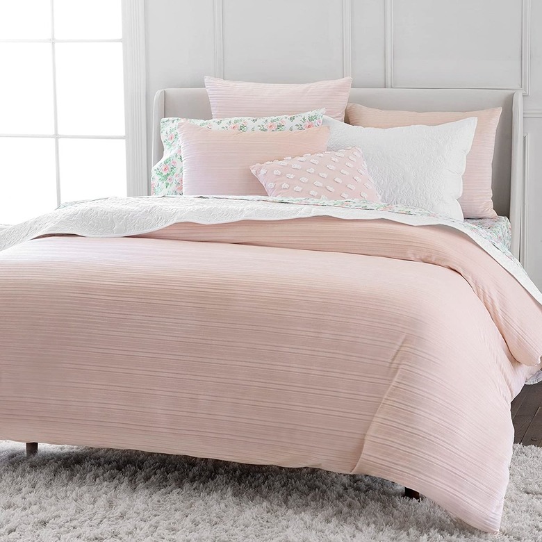 A blush bed: a light pink duvet with three light pink pillows, a green and pink floral pillow and a small blush pillow with white dots.