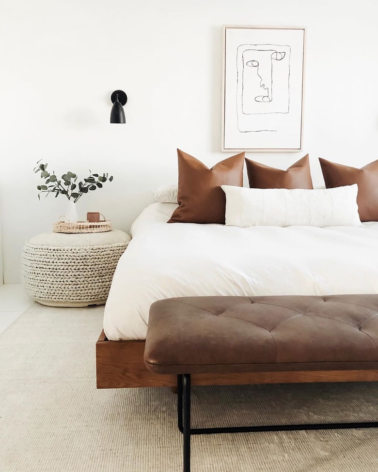 masculine boho bedroom with leather pillows and woven pouf as nightstand