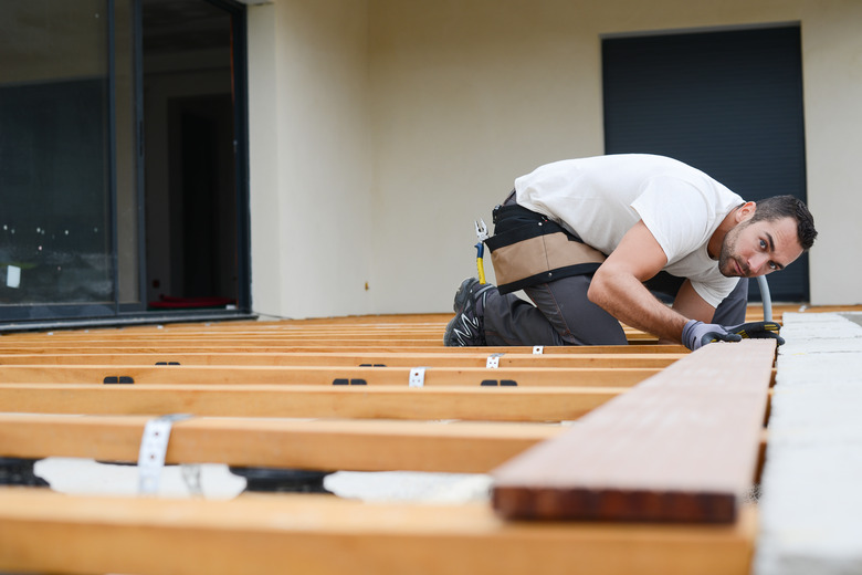 handsome young man carpenter installing a wood floor outdoor terrace in new house construction site