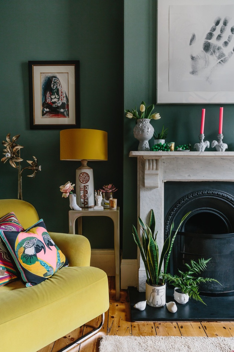 maximalist living room with green walls and vintage marble fireplace next to a yellow velvet armchair