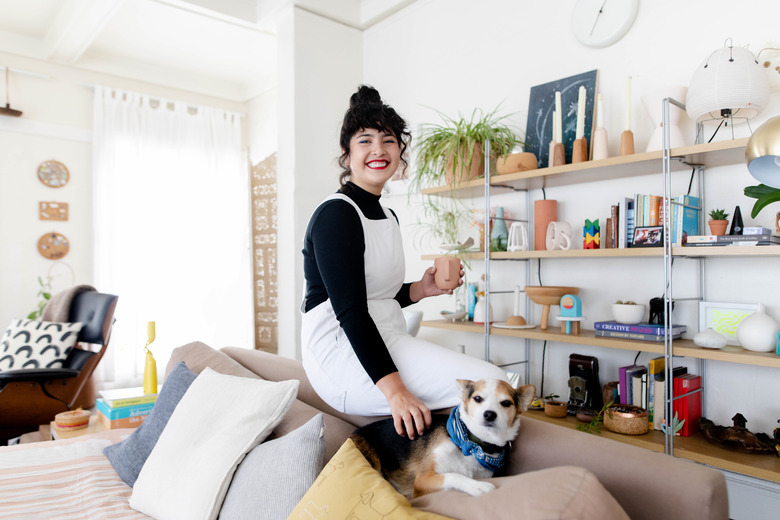 woman sitting on couch edge with dog, shelves nearby