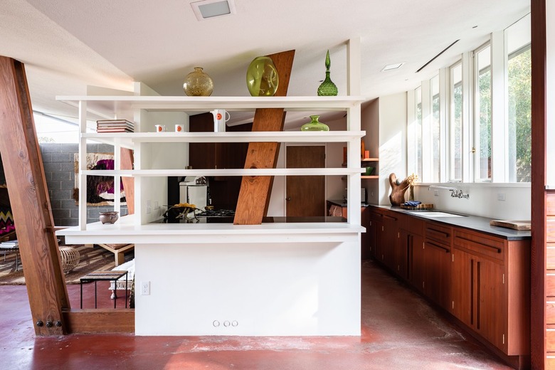 A mid-century home with maroon floors, built-in shelves, wood cabinets and beams