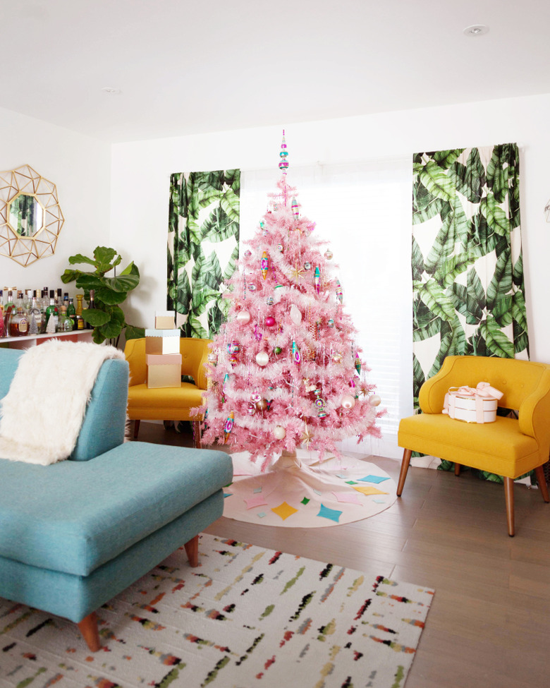 pink midcentury modern Christmas tree with ornaments next to window with tropical drapery