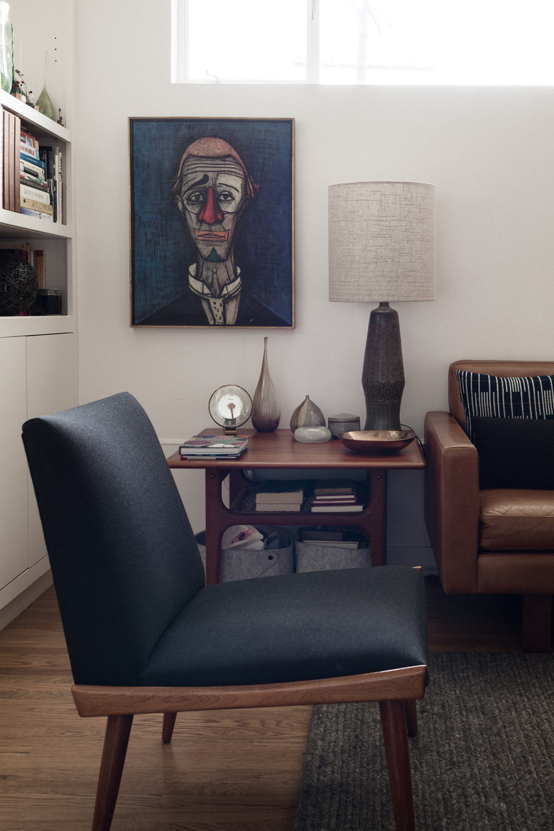 midcentury modern family room with armless sitting chair, coffee leather couch, and abstract clown painting.