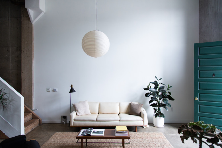 midcentury modern family room with white couch, suspended globe lamp, and teal door.