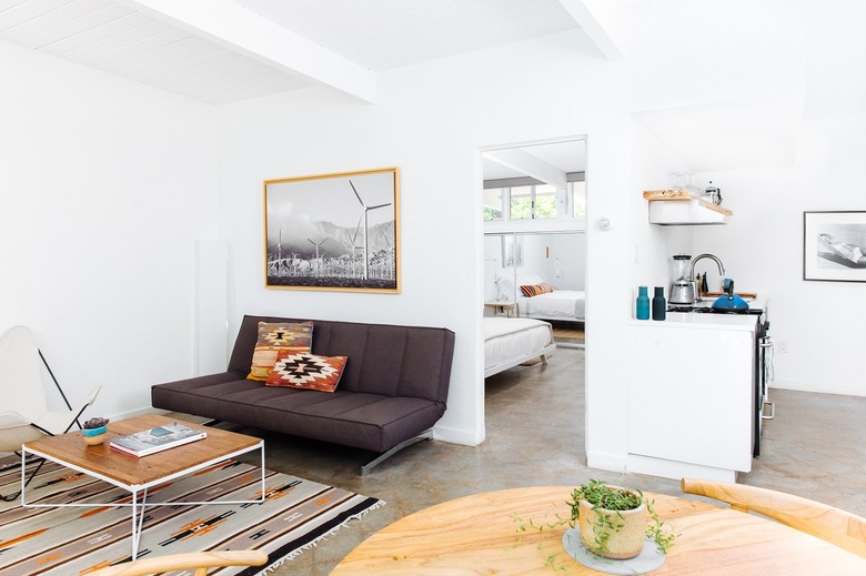 a living room area with a low, brown, mid-century couch, a wooden topped coffee table, and a southwestern rug