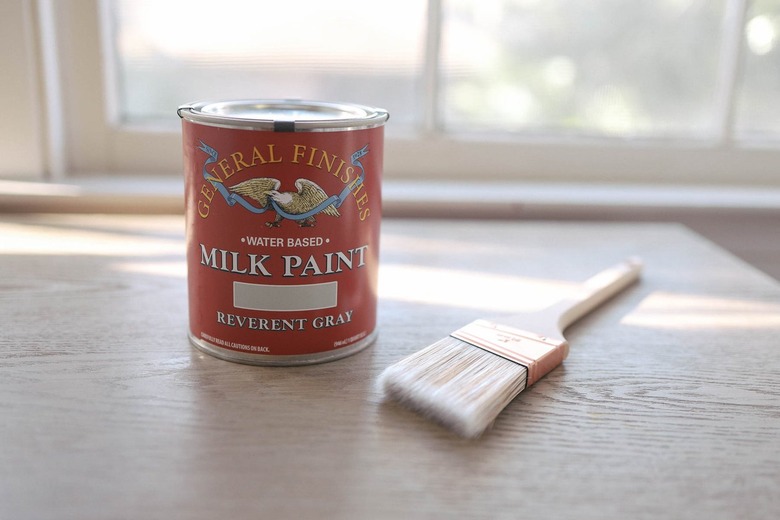 Can of water based milk paint and a paint brush on a wood desk tabletop