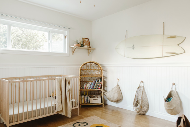 white minimalist nursery decor with wood crib and surf board on the wall