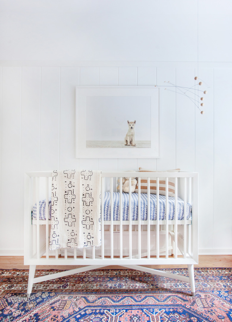 white minimalist nursery decor with colorful vintage rug and white crib