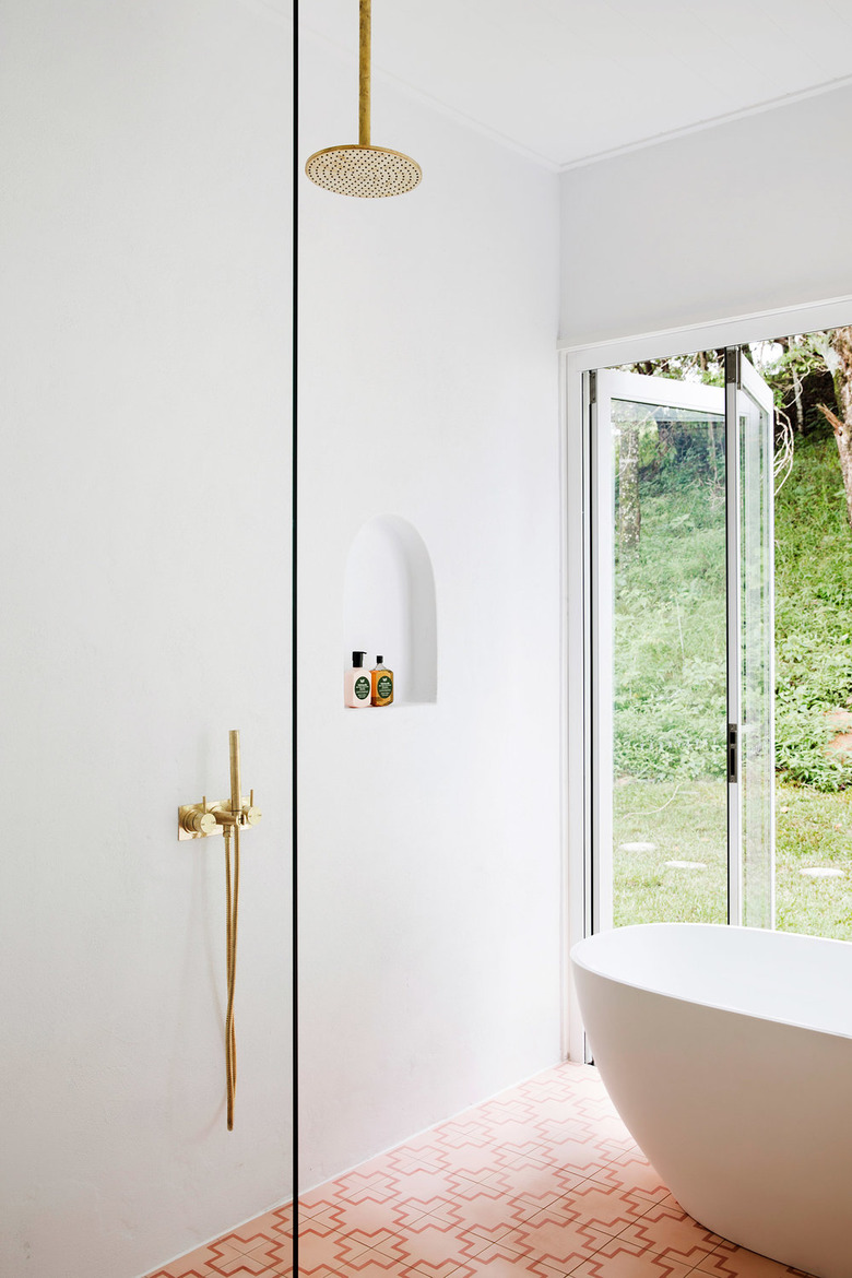 white minimalist shower with brass hardware and pink floor tiles