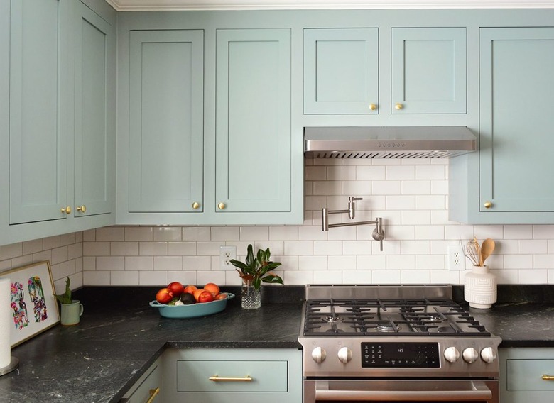 contemporary kitchen with mint green cabinets and white subway tile, black countertops