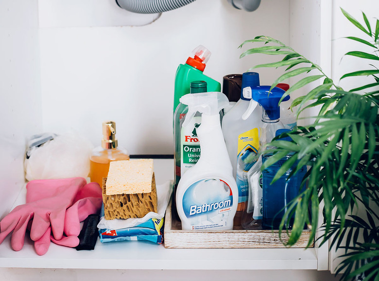 cleaning product bottles, sponges, and pink rubber gloves underneath bathroom sink