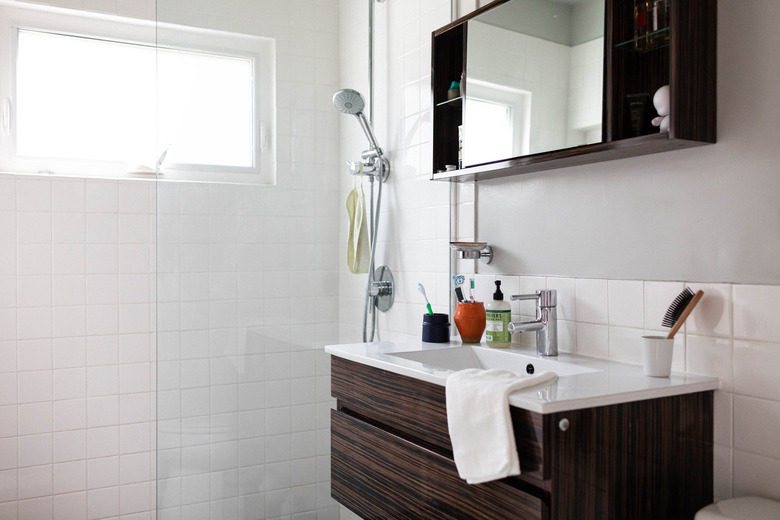 surface-mount wood medicine cabinet with mirror in the center, brown vanity with white ceramic top, white tile shower with glass door