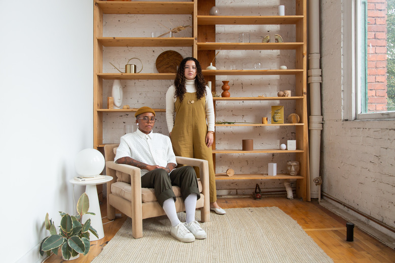 one person sitting and another standing near a shelf