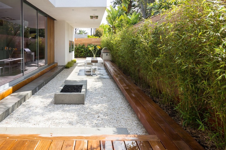 A backyard with a small fire pit surrounded by gravel and wood benches