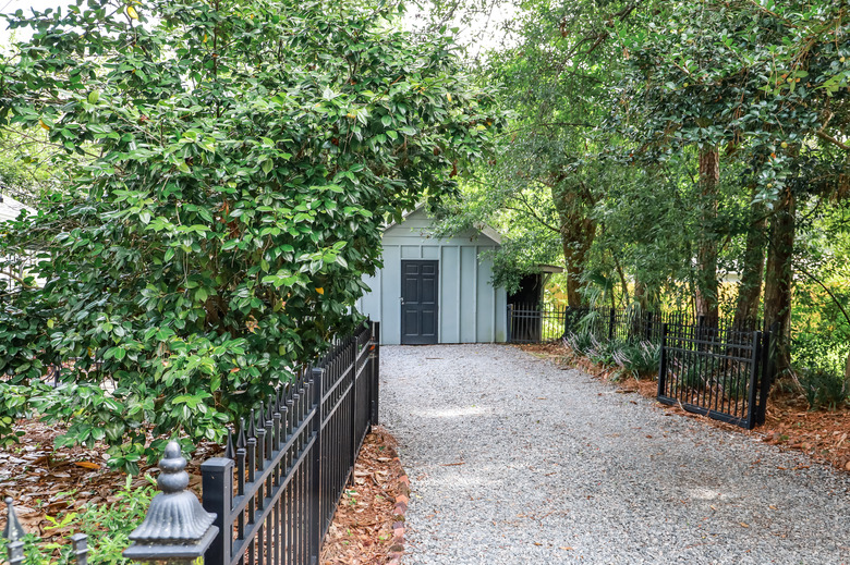 Gravel driveway with fence and blue outdoor shed for storage.