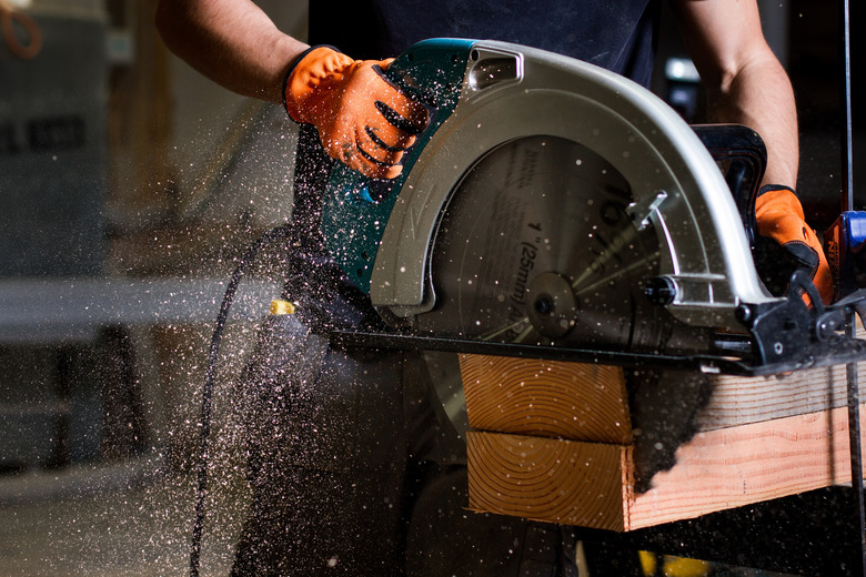 Closeup of carpenter using electric circular saw to cut wood planks.