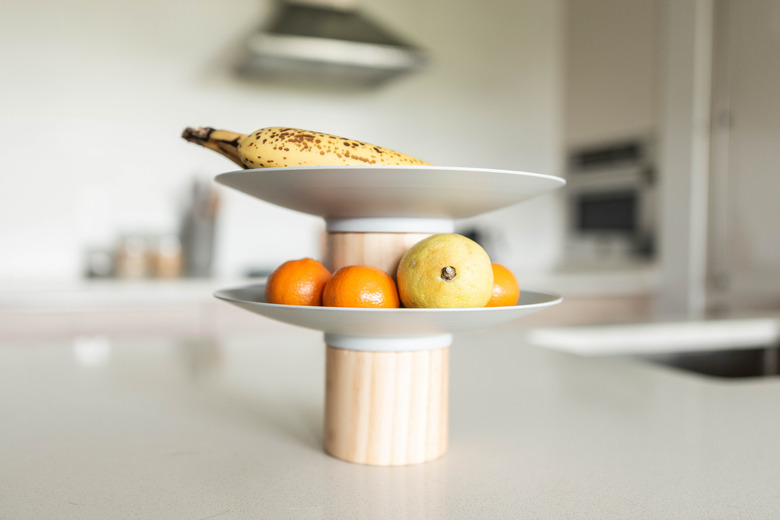 a banana and oranges on a two-tire fruit platter on a white countertop