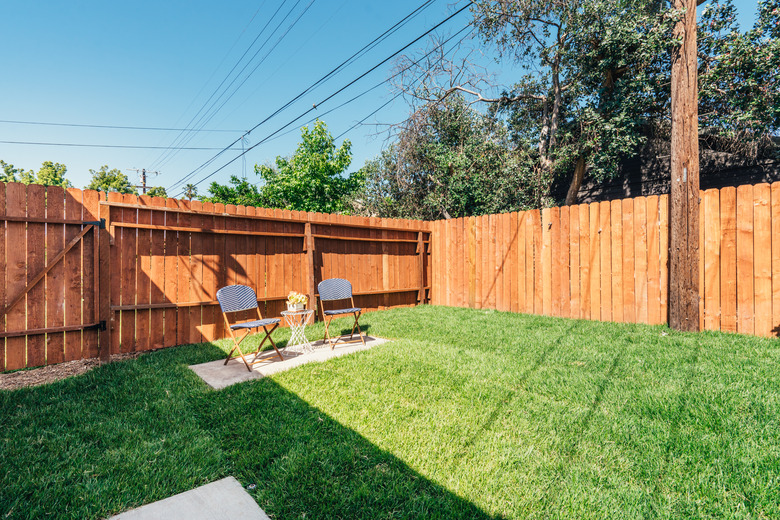 a freshly mowed green yard with two blue lawn chairs; a cedar fence surrounds the yard