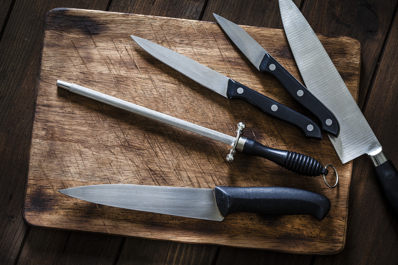 Sharpening steel and various kitchen knives on wooden cutting board