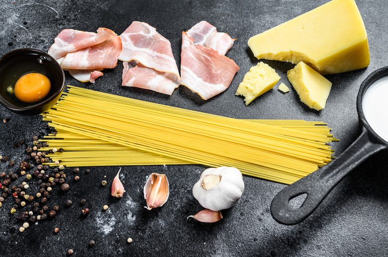 Ingredients for traditional italian pasta alla carbonara. Uncooked spaghetti, pancetta bacon, parmesan cheese, egg. Black background. Top view