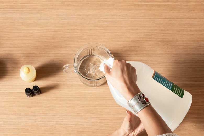 Hand pouring liquid from jug into measuring cup on wooden countertop